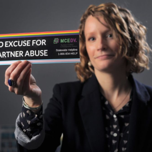 Regina Rooney, communications director for the Maine Coalition to End Domestic Violence, in 2021. Photo by Fred J. Field. regina rooney holds a bumper sticker that reads no excuse for partner abuse