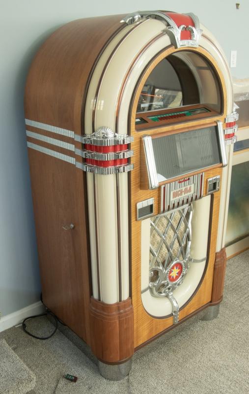 Mr. Belkin’s Custom Replica CD Jukebox by Rock-Ola, in a classic design featuring eight bubble tubes lining the front of the machine and walnut stained wood cabinet, sn 187801, with five internal speakers, a disc loader designed after the older models that played 45 RPM records, and a 100-capacity disc magazine, 60" high, 34" x 24". With manuals and remote control. Mr. Belkin’s Custom Replica CD Jukebox by Rock-Ola, in a classic design featuring eight bubble tubes lining the front of the machine and walnut stained wood cabinet, sn 187801, with five internal speakers, a disc loader designed after the older models that played 45 RPM records, and a 100-capacity disc magazine, 60" high, 34" x 24". With manuals and remote control.